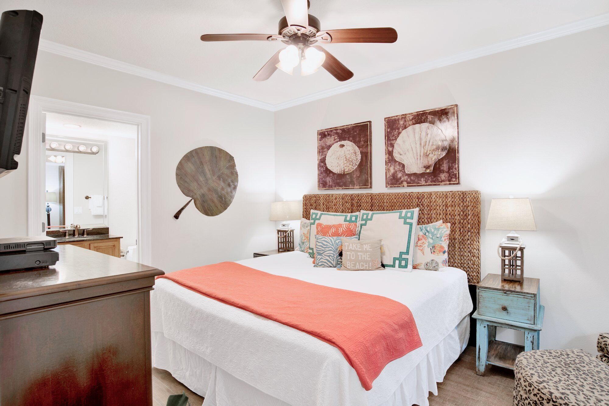 Un dormitorio con cama, ventilador de techo, mesita de noche, lámpara y decoración en la pared.