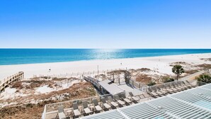 A beach view with a wooden deck and lounge chairs.