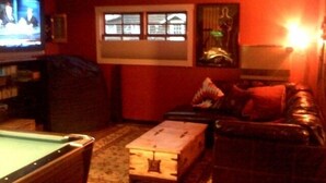 Een woonkamer met een pooltafel, een televisie en een raam met zonwering.