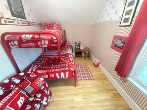 Ein Schlafsaalzimmer mit Etagenbetten, einem Schreibtisch, einem Stuhl, einem Fenster mit Vorhängen und einem Streifenmuster an der Wand.