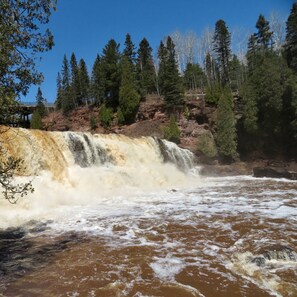 Ein Wasserfall mit einer Brücke im Hintergrund, umgeben von Bäumen.