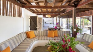 A spacious living area with a large, curved sofa, a wooden ceiling, and a view of the kitchen and outdoor area. - Beachfront House & Pool, 35-meter Oceanfront. Tropical Forest. Surfers' Paradise (Playa Grande)