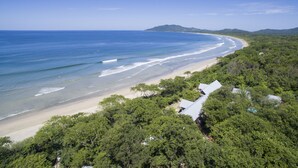 An aerial view of a beach with a sandy shore, surrounded by dense green foliage and a few buildings with sloped roofs. - Beachfront House & Pool, 35-meter Oceanfront. Tropical Forest. Surfers' Paradise (Playa Grande)