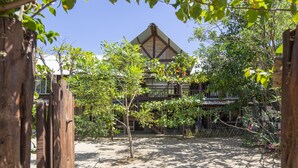 A traditional wooden house with a tiled roof, surrounded by lush greenery and a wooden fence. - Beachfront House & Pool, 35-meter Oceanfront. Tropical Forest. Surfers' Paradise (Playa Grande)