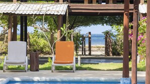 A pool area with two chairs, one white and one orange, and a wooden pergola structure. - Beachfront House & Pool, 35-meter Oceanfront. Tropical Forest. Surfers' Paradise (Playa Grande)
