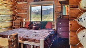Un dormitorio tipo cabaña de madera con cama, cómoda y ventana con vistas a las montañas.