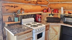 Cocina compacta con estufa, horno y cafetera, que presenta paredes de madera y una encimera de mármol.