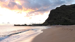 Una playa con un acantilado imponente, mar tranquilo y algunas personas caminando.