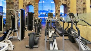 Un gimnasio con paredes de piedra, varias máquinas de ejercicio y grandes ventanales con vistas.