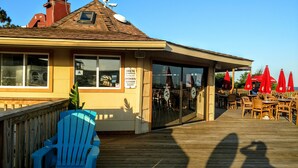 A building with a wooden deck, outdoor seating with red umbrellas, and a sign indicating gender-specific restroom directions. - Admiral’s Row B2 - 2nd floor corner condo.  Clean, comfy and relaxing (Hilton Head Island)