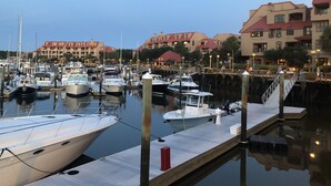 A marina with boats docked, wooden walkways, and buildings with red roofs in the background. - Admiral’s Row B2 - 2nd floor corner condo.  Clean, comfy and relaxing (Hilton Head Island)