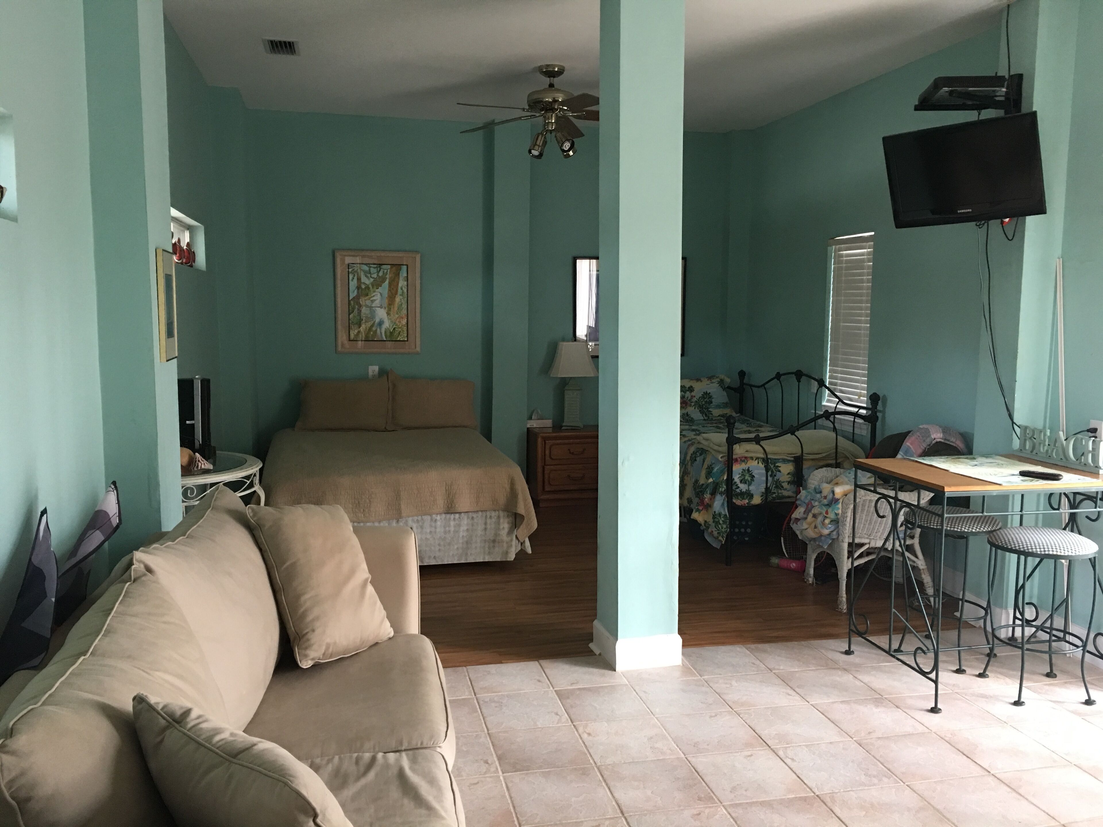 A room with a bed, a desk, a TV, and a ceiling fan.