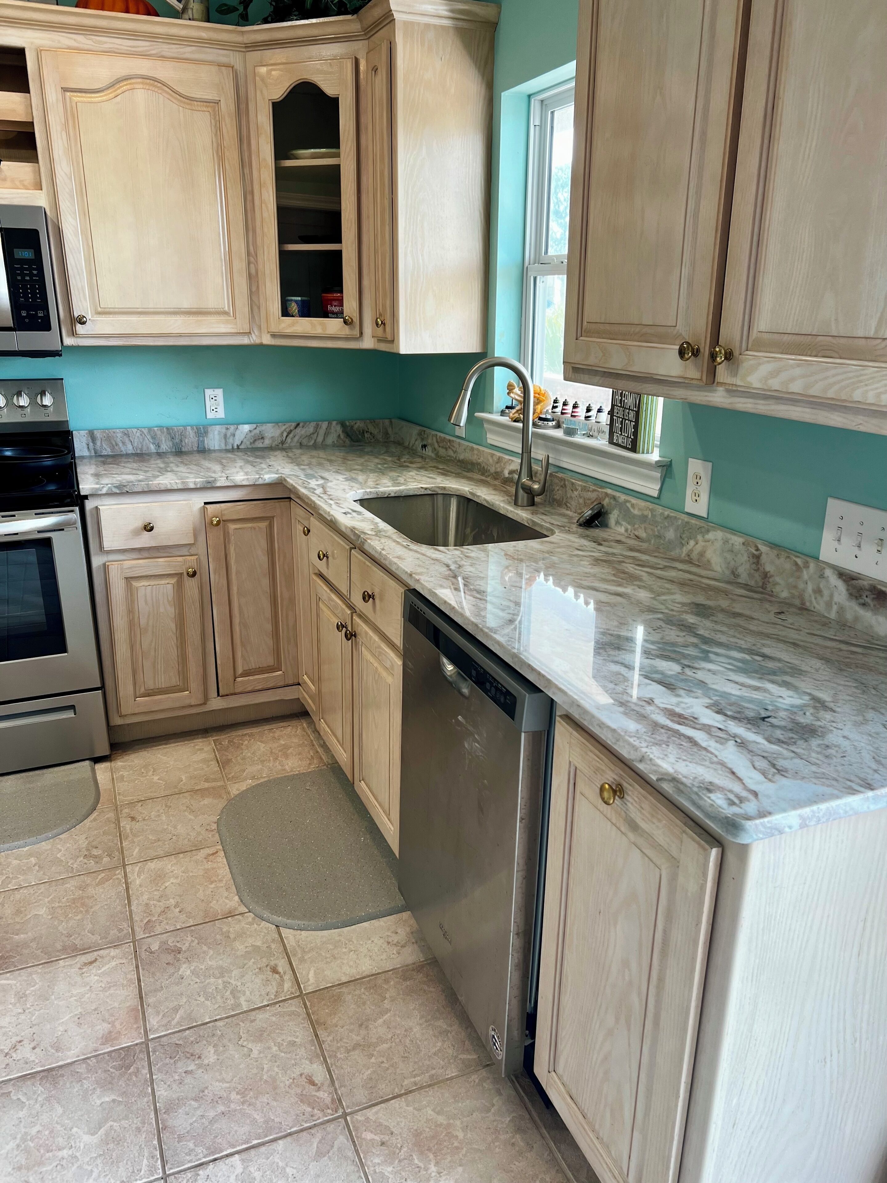 A kitchen with wooden cabinets, a stainless steel dishwasher, and a marble countertop.