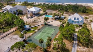 Vue aérienne d’une propriété située sur la côte, comprenant plusieurs bâtiments, un court de tennis et une plage.