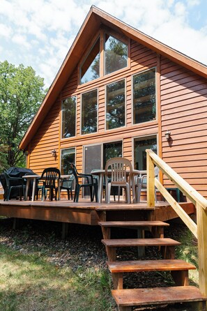 A wooden cabin with a deck, outdoor seating, and a staircase leading to the entrance.