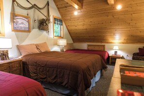 A cozy, rustic bedroom with a sloped ceiling, wooden beams, and a bed with a red blanket.