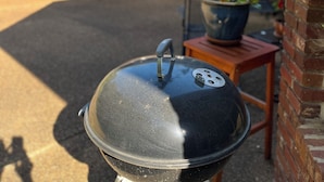 A barbecue grill in a backyard with a brick house in the background.