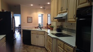 A kitchen with light wooden cabinets, a black refrigerator, a stove, and a window with a view of the outside.