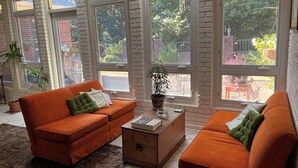 A spacious living room with large windows, a brick wall, and a cozy orange sofa set.