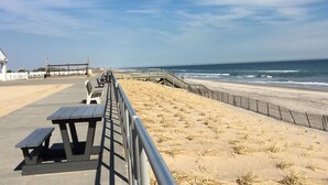Una spiaggia con una passerella in legno, tavoli da picnic e una recinzione.