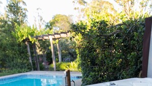 A hot tub with a wooden deck and a pool in the background.