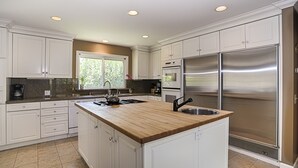 A modern kitchen with white cabinetry, a wooden island, stainless steel appliances, and a window providing natural light.