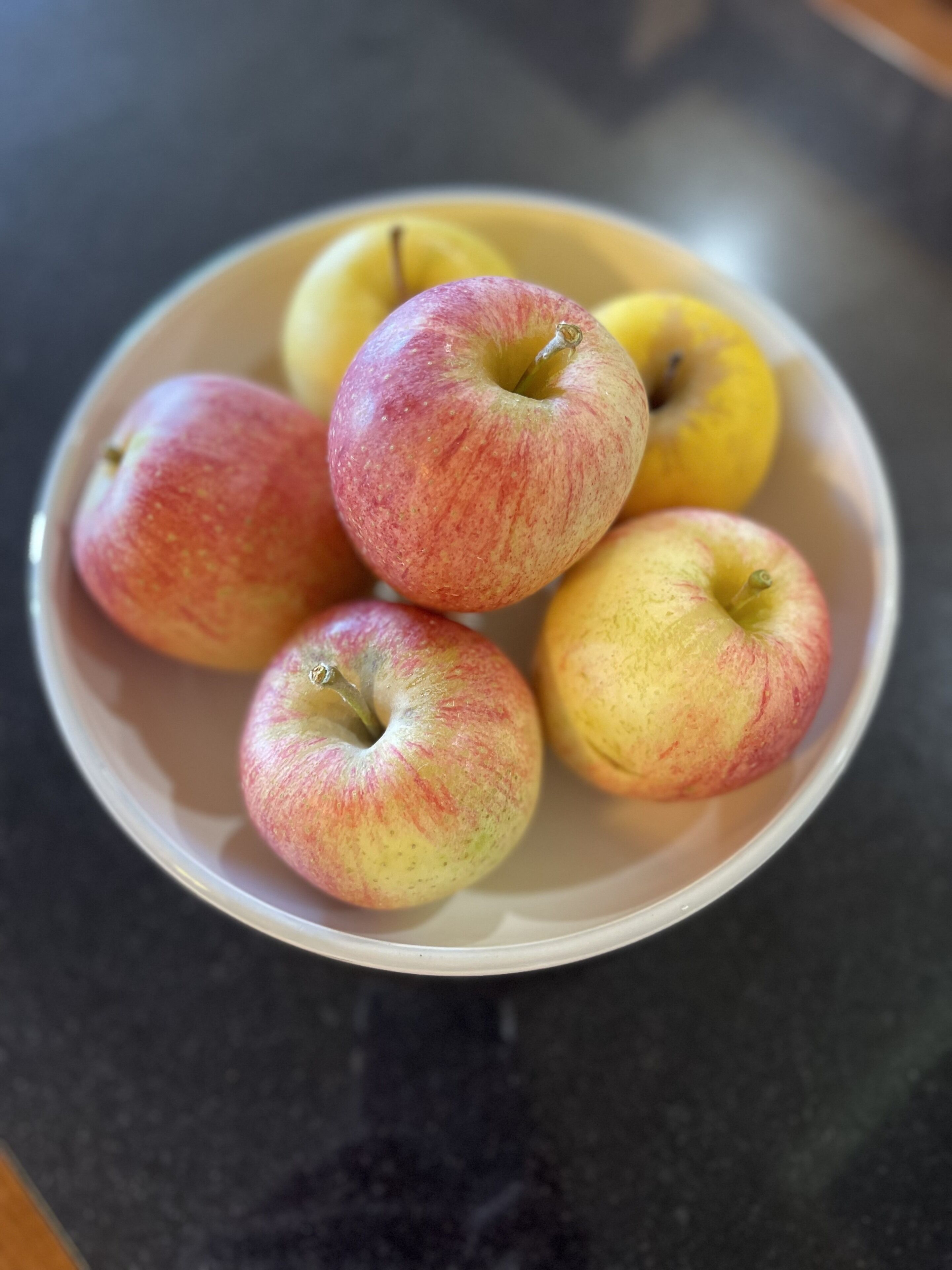 En skål med äpplen på en mörk bänkskiva.