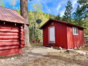 A red wooden cabin with a door and window, surrounded by trees and a gravel path. - Cozy Cabin on Florida River- 15 mins from Downtown (Durango)