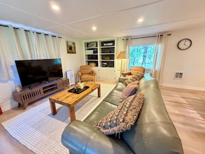 Uma sala de estar com um sofá de couro, uma mesa de centro de madeira, uma televisão e uma estante de livros.