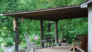 A covered outdoor seating area with wooden furniture, surrounded by lush greenery.