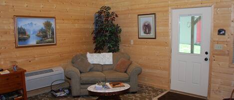 Una habitación acogedora con paredes de madera, un sofá, una mesita de café, una puerta y una ventana.
