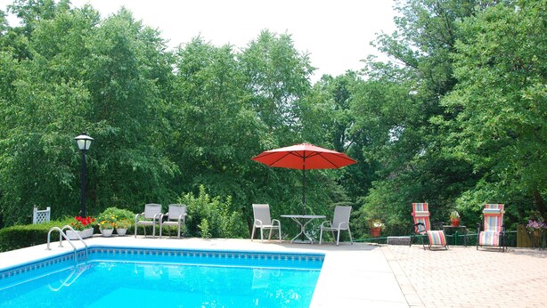 A swimming pool with a red umbrella, surrounded by chairs and potted plants.