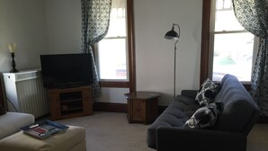 Una sala de estar con un sofá, un televisor, una lámpara y una ventana con cortinas.