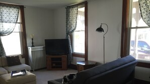 Una sala de estar con un sofá, un televisor sobre un mueble, una lámpara y un radiador.