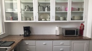 Una cocina con armarios blancos, un microondas, una cafetera y diferentes platos y utensilios.