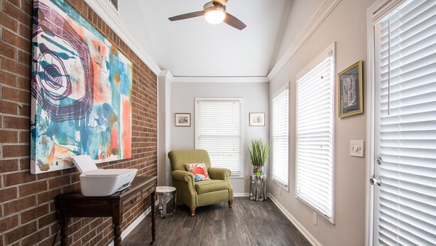 A hallway with a brick wall, a green armchair, a ceiling fan, and a large abstract painting. - Winter Discounts/We love pets! 6ft fenced in backyard and pet amenities. (Hanahan)