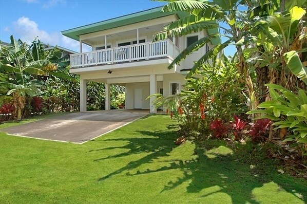 A two-story house with a balcony, surrounded by lush greenery and a well-maintained lawn.