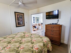 Quarto com cama, cômoda, televisão e porta que dá para outro espaço.