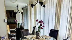 Une salle à manger avec une table à plateau de verre, des chaises à motifs floraux, un vase d’orchidées et un lustre.
