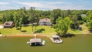 Una casa grande con muelle y barco, rodeada de abundante vegetación y un lago.