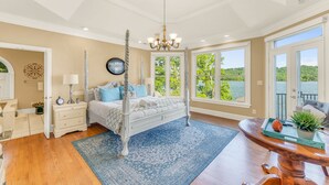 Un dormitorio con cama con dosel, candelabro, ventana grande con vista a vegetación y suelo de madera.