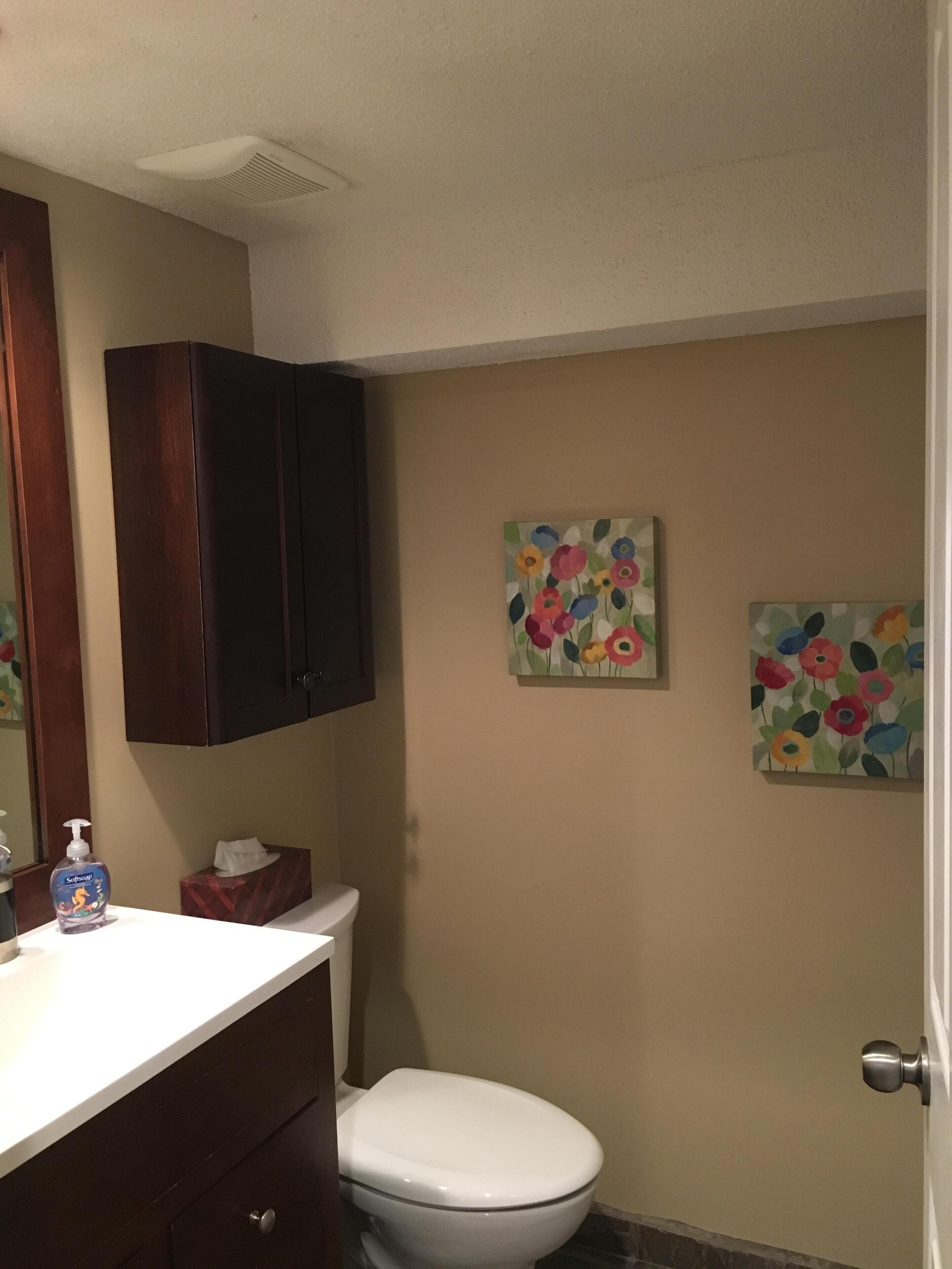 A bathroom with a white toilet, a wooden cabinet, and two floral paintings on the wall.