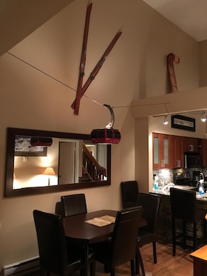 Uma sala de jantar com mesa e cadeiras, um espelho e um suporte para esquis no teto.