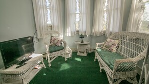 Una habitación con dos sofás de mimbre, una mesita redonda pequeña, un televisor y una alfombra verde.