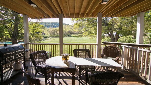 Un patio techado al aire libre con una mesa, sillas, una parrilla y vistas a un paisaje verde.