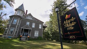 Una casa de estilo victoriano con una torre destacada y un cartel que anuncia Maple Shade Villa, ofreciendo servicios de alojamiento y desayuno.