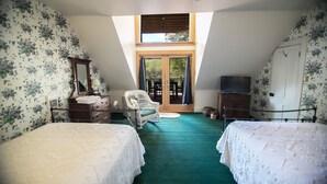 Un dormitorio con dos camas, una silla, un tocador, una televisión y una puerta al balcón.
