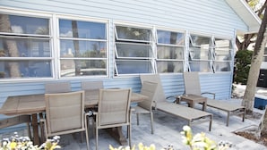 An outdoor patio with a wooden table and chairs, a bench, and a blue house in the background. - Cozy and friendly. All is Well - no damage (Clearwater Beach)