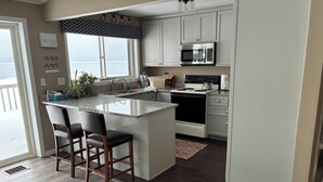 A modern kitchen with a large island, bar stools, a microwave, and an oven.