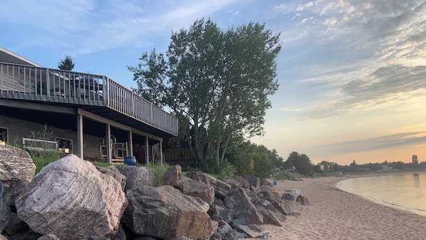 A beach house with a wooden deck and large rocks in front.